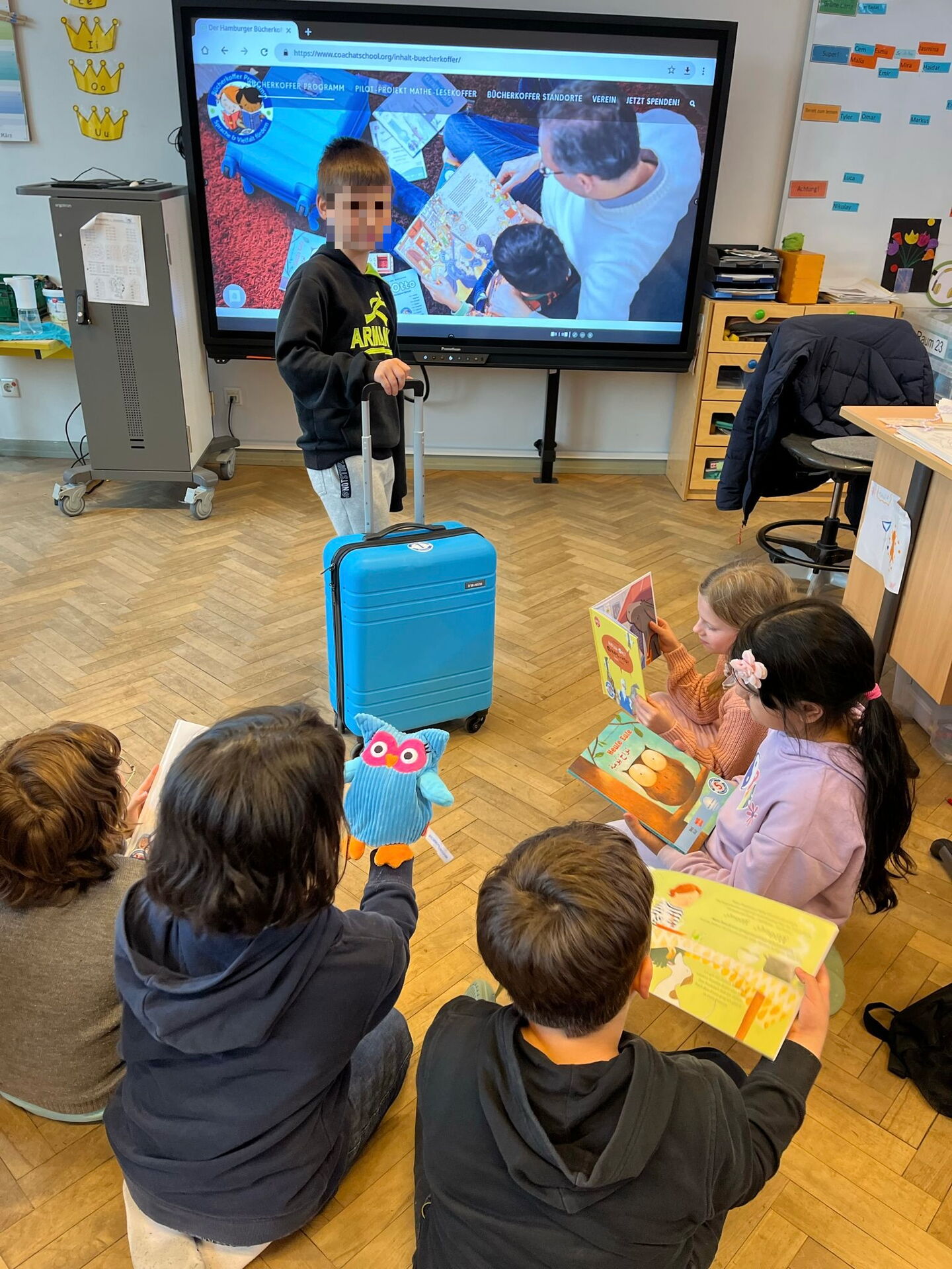 Schüler hält den Bücherkoffer fest und andere Schülerinnen und Schüler sitzen lesend im Kreis um ihn herum