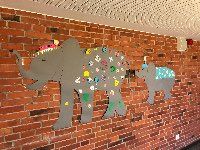 Mama-Elefant mit bunten Verzierungen und Baby-Elefant mit blau-gelber Sternendecke marschieren an der Wand