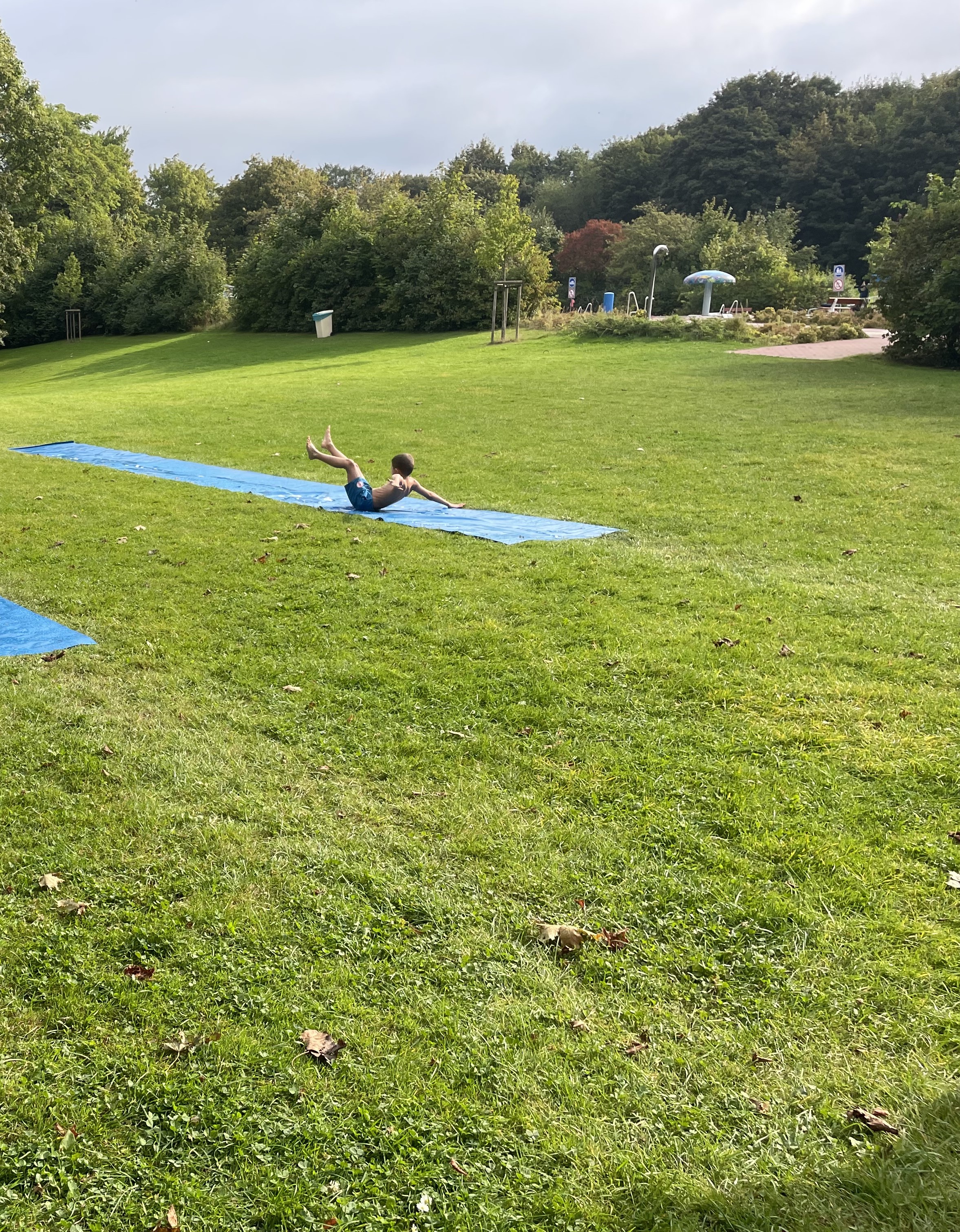 Ein Junge rutscht auf dem Po über die Seifenwassermatte. 